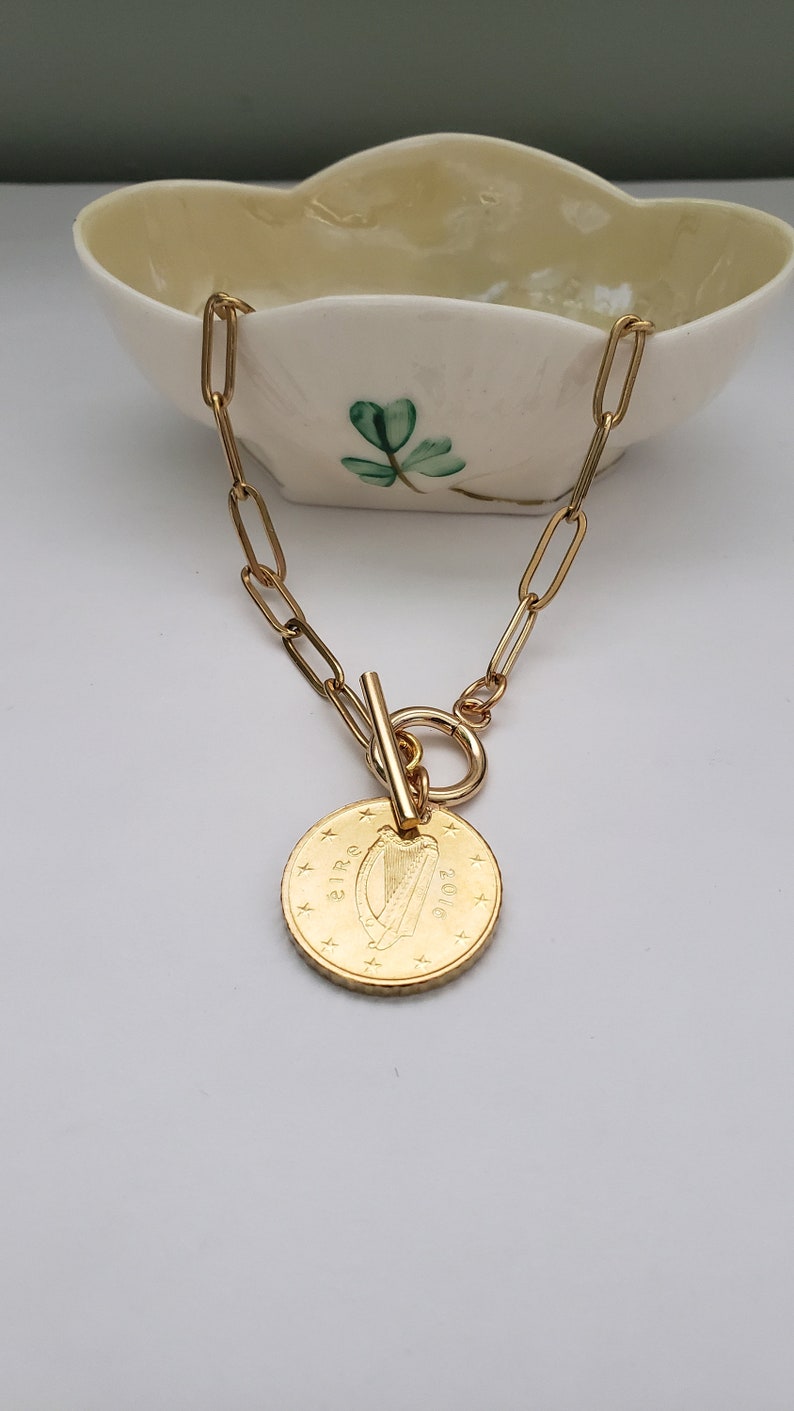 May include: A gold chain necklace with a gold coin pendant featuring the Irish harp and the word "EIR" and the year "2016".