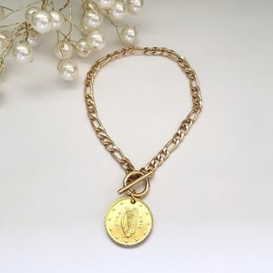 May include: A gold chain bracelet with a toggle clasp and a gold coin charm featuring the Irish harp and the year 2018.