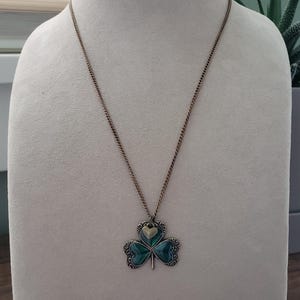 May include: A gold chain necklace with a green shamrock pendant. The shamrock is made of three heart-shaped leaves with a gold heart in the centre.