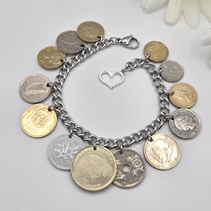 Pode incluir: Uma pulseira de berloques com uma corrente de metal prateado, um fecho lagosta e um pingente central em forma de cora&ccedil;&atilde;o. A pulseira &eacute; adornada com v&aacute;rias moedas internacionais em tons de dourado e prateado, com textos e imagens vis&iacute;veis.