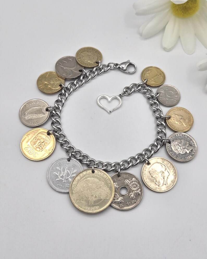Pode incluir: Uma pulseira de berloques com uma corrente de metal prateado, um fecho lagosta e um pingente central em forma de cora&ccedil;&atilde;o. A pulseira &eacute; adornada com v&aacute;rias moedas internacionais em tons de dourado e prateado, com textos e imagens vis&iacute;veis.