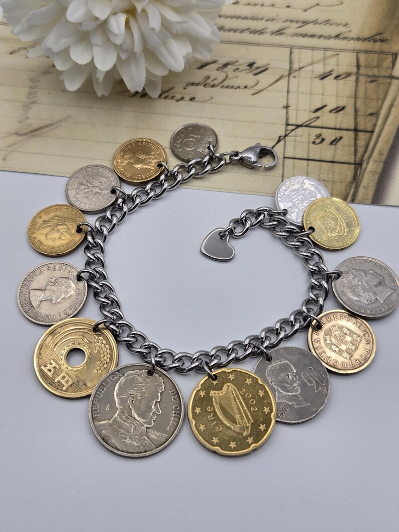 Pode incluir: Uma pulseira de elos de metal prateado com uma cole&ccedil;&atilde;o de v&aacute;rias moedas internacionais como berloques. As moedas variam em tamanho, cor e acabamento met&aacute;lico, incluindo tons dourados e prateados. Um pequeno berloque em forma de cora&ccedil;&atilde;o est&aacute; preso.