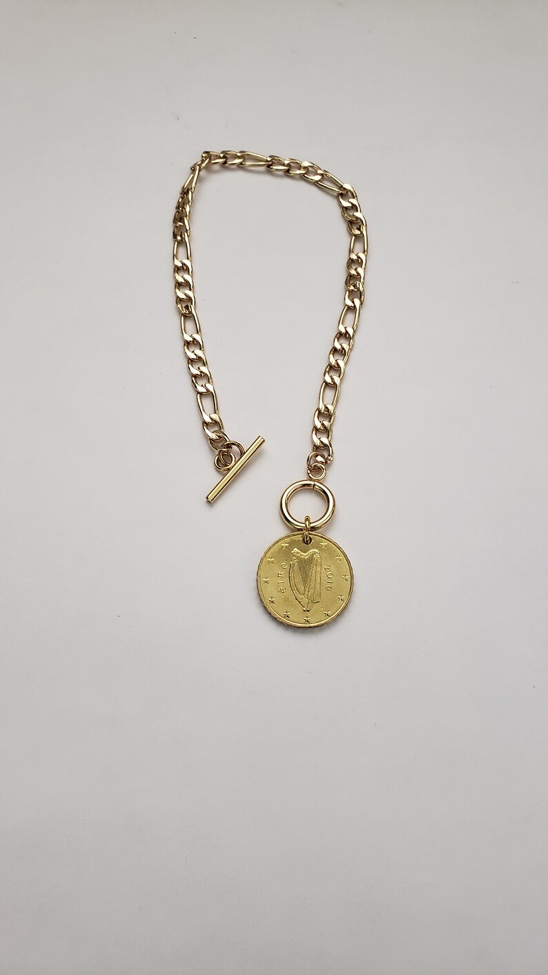 May include: A gold chain necklace with a gold coin pendant featuring the Irish harp and the text "&euro;1 EURO 2002".
