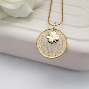 May include: Gold necklace with a 2002 Irish Euro coin pendant featuring a harp and a gold four-leaf clover charm.
