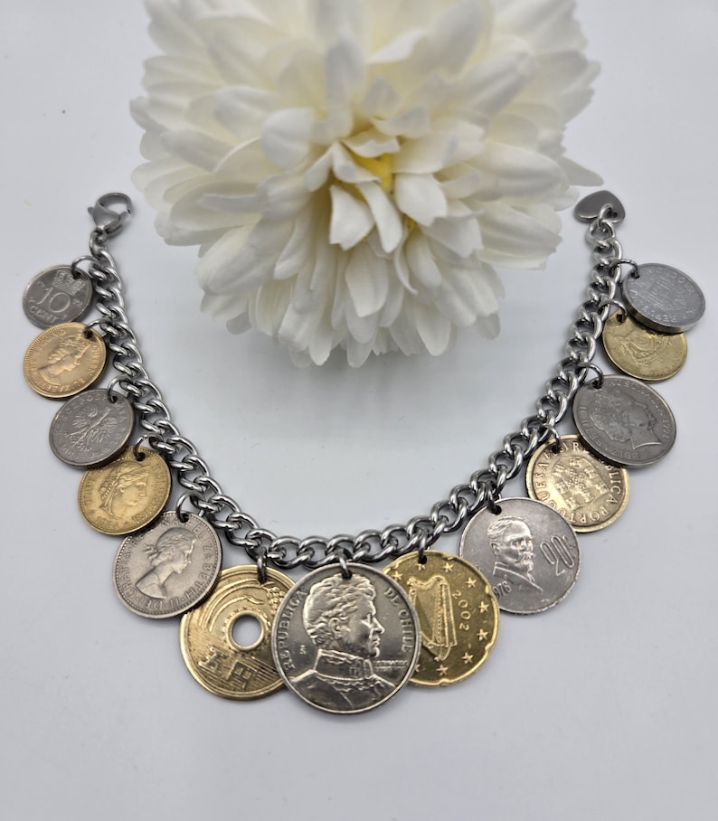 Pode incluir: Uma pulseira de berloques com uma corrente de metal prateado adornada com v&aacute;rias moedas internacionais em tons de dourado e prateado. As moedas exibem diversos retratos, s&iacute;mbolos e textos, incluindo 10 CENT, 20, 2002 e REPUBLICA DE CHILE.