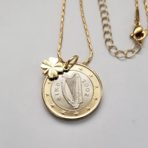May include: A gold chain necklace with a gold shamrock charm and a 2002 Irish euro coin pendant featuring a harp.