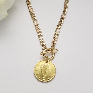 May include: A gold chain necklace with a toggle clasp and a gold coin pendant featuring the Irish harp and the year 2016.