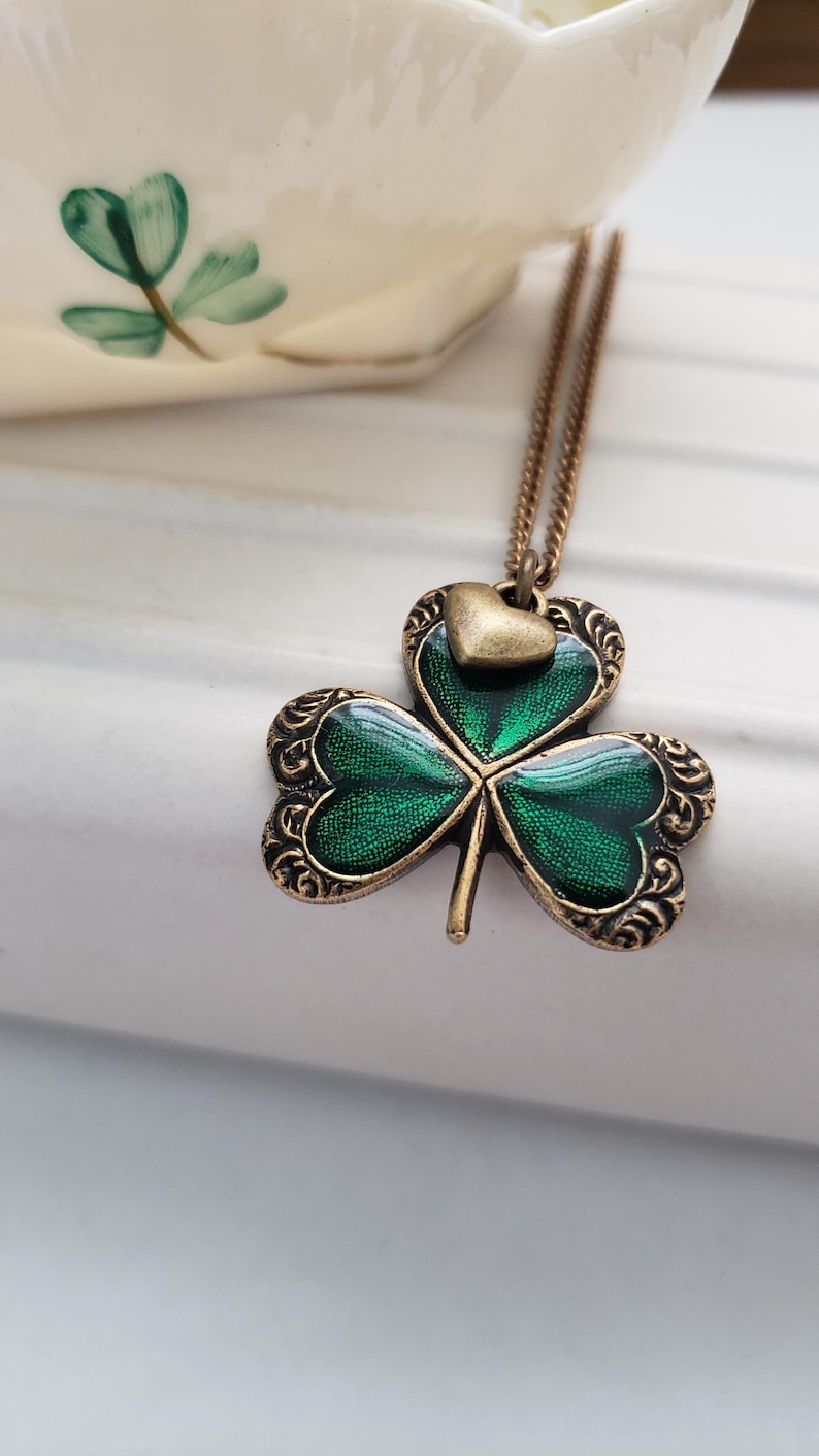 May include: A gold chain necklace with a green shamrock pendant. The shamrock has a small gold heart charm on top.