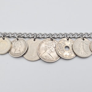 K&ouml;nnte beinhalten: Ein silbernes Kettenarmband mit verschiedenen Vintage-M&uuml;nzen als Anh&auml;nger. Die M&uuml;nzen, in verschiedenen Gr&ouml;&szlig;en und Designs, sind mit kleinen Schlaufen an der Kette befestigt. Das Armband wird vor einem schlichten wei&szlig;en Hintergrund pr&auml;sentiert.
