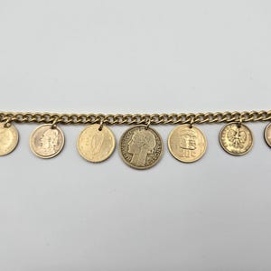 May include: A gold-toned chain link bracelet featuring seven dangling circular coin charms of varying sizes and designs. The central coin displays a profile portrait and the text REPUBLIQUE FRANCAISE. The other coins show various national emblems.