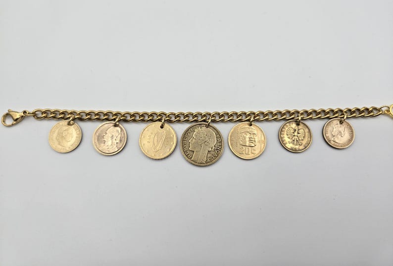 May include: A gold-toned chain link bracelet featuring seven dangling circular coin charms of varying sizes and designs. The central coin displays a profile portrait and the text REPUBLIQUE FRANCAISE. The other coins show various national emblems.