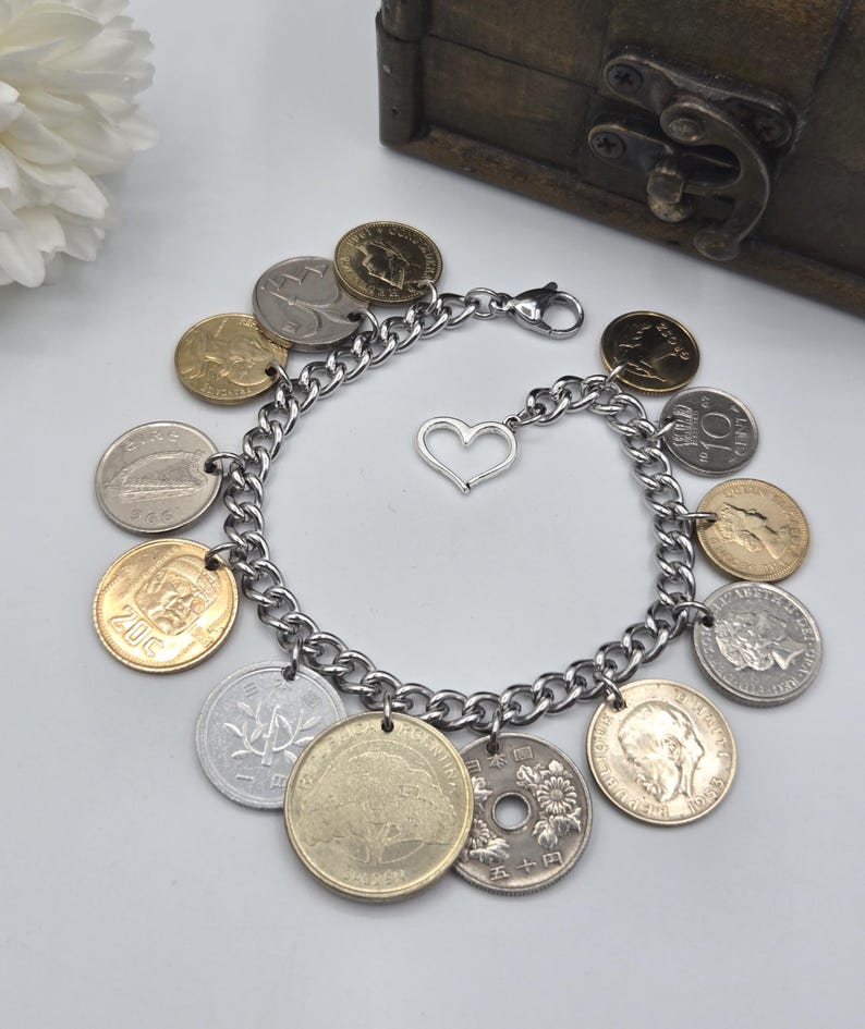 Pode incluir: Uma pulseira de elos em tom prateado com v&aacute;rias moedas internacionais como berloques. A pulseira inclui um pequeno berloque em forma de cora&ccedil;&atilde;o prateado e um fecho lagosta. As moedas variam na cor, incluindo tons de ouro, prata e bronze, e apresentam diversos retratos, s&iacute;mbolos e textos.