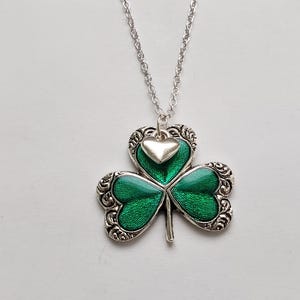 May include: A silver chain necklace with a green shamrock pendant. The shamrock has a small silver heart charm in the centre.