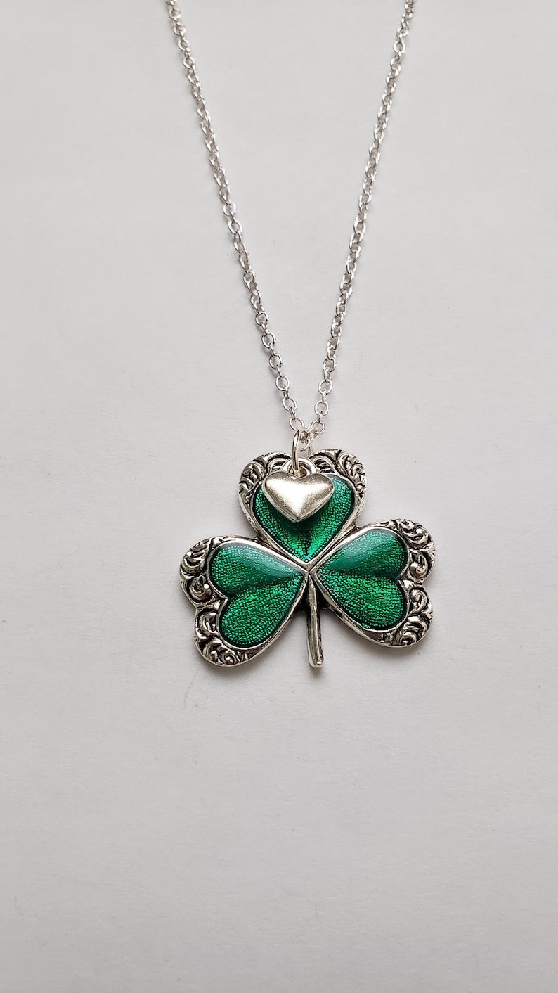 May include: A silver chain necklace with a green shamrock pendant. The shamrock has a small silver heart charm in the centre.