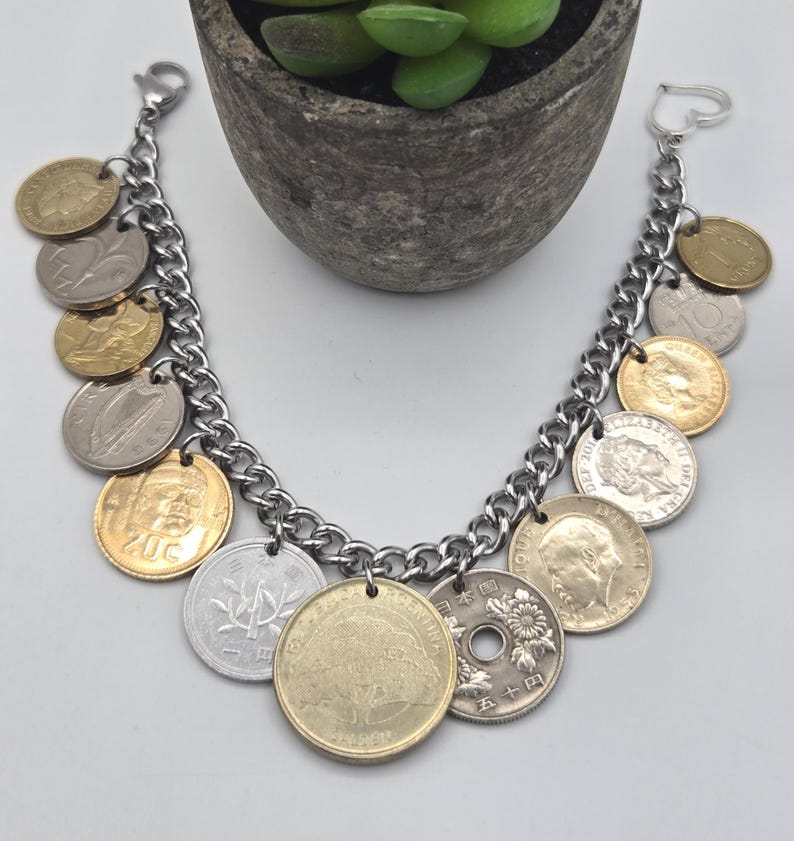 Pode incluir: Uma pulseira de corrente de metal prateado com uma cole&ccedil;&atilde;o de v&aacute;rias moedas internacionais como pingentes. As moedas variam em cor, incluindo tons de ouro, prata e bronze, e apresentam diversos desenhos, retratos e textos de v&aacute;rios pa&iacute;ses.