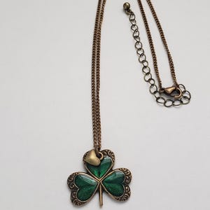May include: A gold chain necklace with a green shamrock pendant. The shamrock has a small gold heart charm at the top.