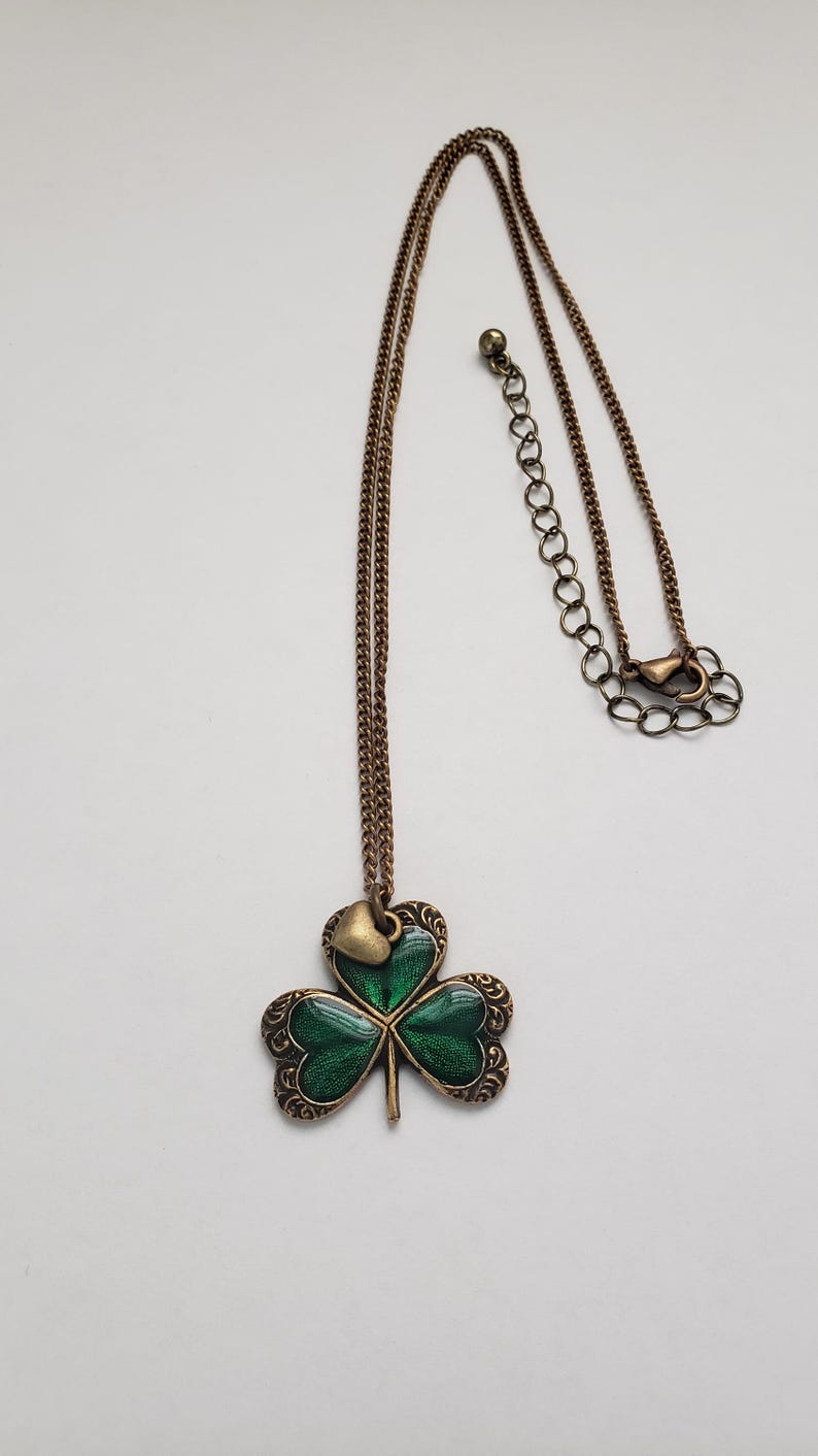 May include: A gold chain necklace with a green shamrock pendant. The shamrock has a small gold heart charm at the top.