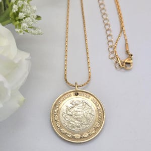 K&ouml;nnte beinhalten: Eine goldfarbene Halskette mit einem runden Anh&auml;nger aus einer mexikanischen M&uuml;nze. Die M&uuml;nze zeigt ein silberfarbenes Zentrum mit einem Adleremblem und einen goldfarbenen Rand mit dem Text "ESTADOS UNIDOS MEXICANOS".