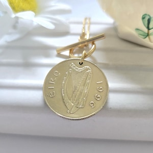 May include: Gold necklace with a 1996 Irish Euro coin pendant featuring a harp. The coin is attached to a gold toggle clasp.
