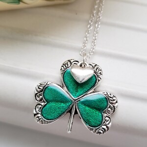 May include: A silver necklace with a green shamrock pendant. The shamrock has a silver heart charm on top.