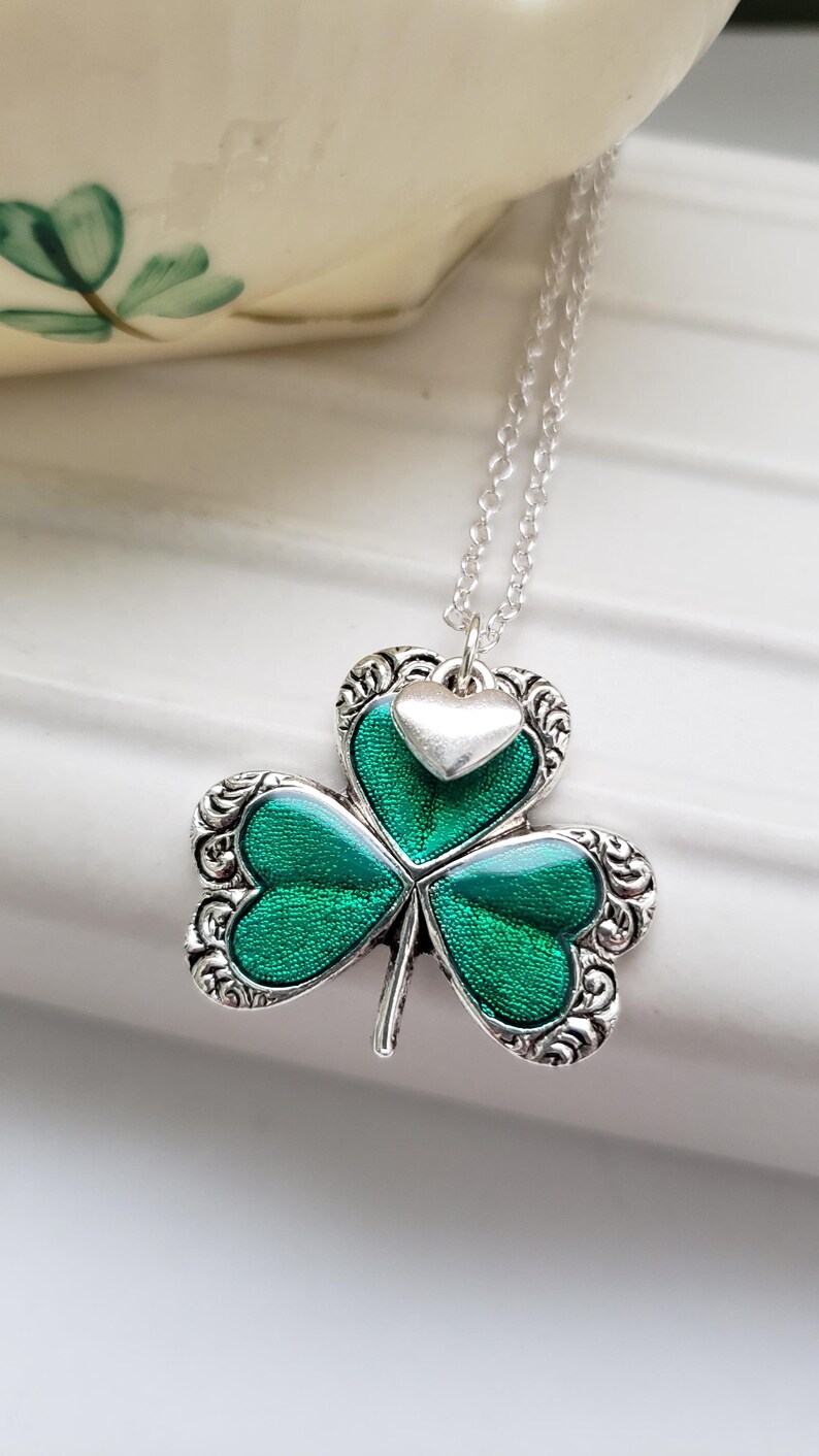 May include: A silver necklace with a green shamrock pendant. The shamrock has a silver heart charm on top.