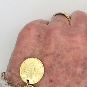 May include: A gold bracelet with a gold coin charm featuring a harp and the text "Euro 2016".