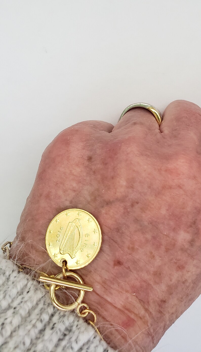May include: A gold bracelet with a gold coin charm featuring a harp and the text "Euro 2016".
