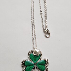 May include: A silver chain necklace with a green shamrock pendant. The shamrock is detailed with silver scrollwork and has a green enamel finish.