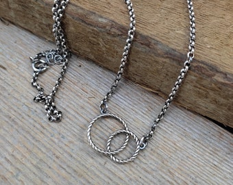 May include: A silver chain necklace with a double circle pendant. The circles are intertwined and have a rope-like texture.