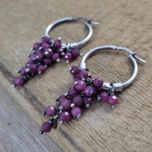 Könnte beinhalten: Ein Paar silberne Creolen mit herabhängenden Trauben aus violetten Edelsteinperlen.