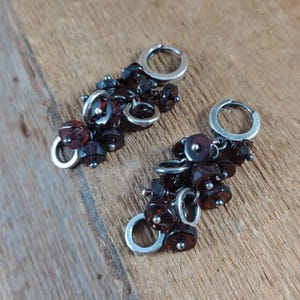 Pode incluir: Um par de brincos de argola com argolas de prata e v&aacute;rias contas de pedras preciosas de cor vermelho escuro.