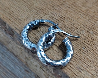 May include: A pair of silver hoop earrings with a hammered texture. The earrings are small and delicate, and they have a simple, elegant design.