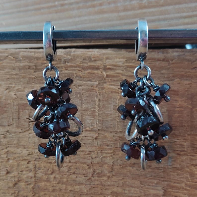 Pode incluir: Um par de brincos de argola de prata com cachos pendentes de pedras preciosas de cor vermelho escuro.