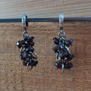 Pode incluir: Um par de brincos de argola de prata com cachos pendurados de pedras preciosas de cor castanho escuro. Os brincos est&atilde;o suspensos de uma barra de prata.