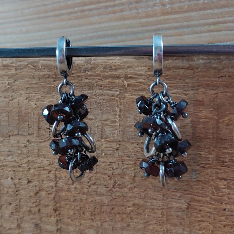 Pode incluir: Um par de brincos de argola de prata com cachos pendurados de pedras preciosas de cor castanho escuro. Os brincos est&atilde;o suspensos de uma barra de prata.