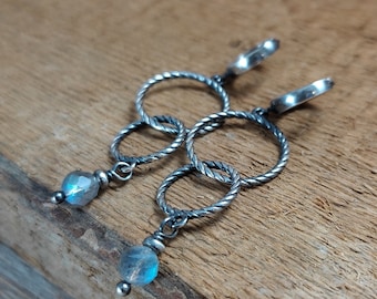 Peut inclure: Boucles d'oreilles créoles en argent avec une pierre précieuse bleue irisée suspendue. Les créoles sont torsadées et présentent un design délicat et complexe.