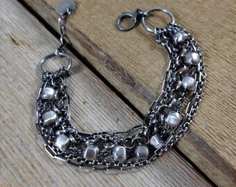 May include: A silver bracelet with multiple chains and small, round beads. The bracelet has a clasp closure.