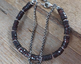 May include: A dark red gemstone bracelet with a silver chain and clasp. The bracelet is made of faceted, round beads.