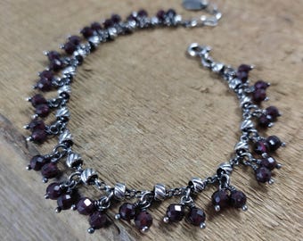 May include: A silver chain bracelet with dangling garnet beads. The bracelet has a silver clasp.