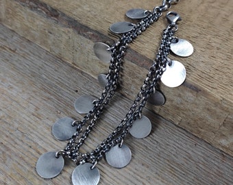 May include: A silver chain bracelet with multiple strands and dangling round charms. The bracelet is made of oxidized silver and has a rustic, vintage look.