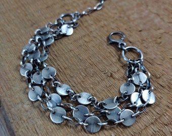 May include: A silver bracelet with three rows of round, flat, silver discs connected by silver chain links.