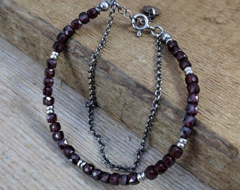 May include: A silver chain bracelet with dark red gemstone beads. The bracelet has a silver clasp.