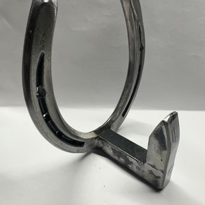 May include: A silver horseshoe shaped metal hook with a single hook on the bottom. The hook is designed to be mounted on a wall.