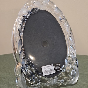 May include: Clear glass photo frame with a floral design. The frame has an oval opening and a black backing. The frame is labeled "Classic Memories" and "MIKASA".