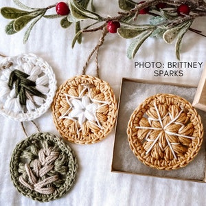 Puede incluir: Cuatro adornos de ganchillo en diferentes colores y patrones. Los adornos son blancos, verdes y amarillos con detalles blancos. Los adornos cuelgan de una cuerda y est&aacute;n sobre un fondo blanco. El texto "PHOTO: BRITTNEY SPARKS" est&aacute; en la esquina superior derecha de la imagen.