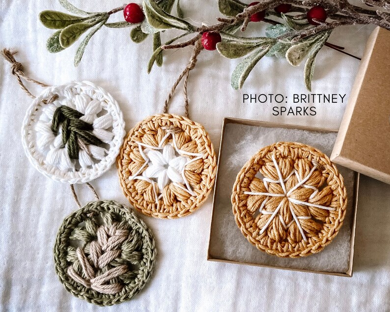 Puede incluir: Cuatro adornos de ganchillo en diferentes colores y patrones. Los adornos son blancos, verdes y amarillos con detalles blancos. Los adornos cuelgan de una cuerda y est&aacute;n sobre un fondo blanco. El texto "PHOTO: BRITTNEY SPARKS" est&aacute; en la esquina superior derecha de la imagen.