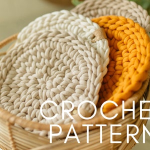 Pode incluir: Três tapetes de crochê em uma cesta de vime. Os tapetes são bege, marrom claro e laranja. O texto "CROCHET PATTERN" está sobreposto à imagem.