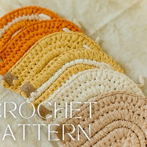 Pode incluir: Um conjunto de bases para copos em croché semicirculares dispostas em leque, com um gradiente de cores do laranja escuro ao amarelo, creme e bege. Cada peça tem uma pequena etiqueta de couro com o texto CROCHET PATTERN.