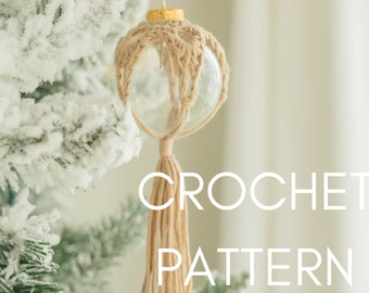 Puede incluir: Un adorno de crochet con un borla que cuelga de un árbol de Navidad nevado. El adorno está hecho de hilo beige y está envuelto alrededor de una bola de vidrio transparente. El texto "CROCHET PATTERN" es visible en la imagen.