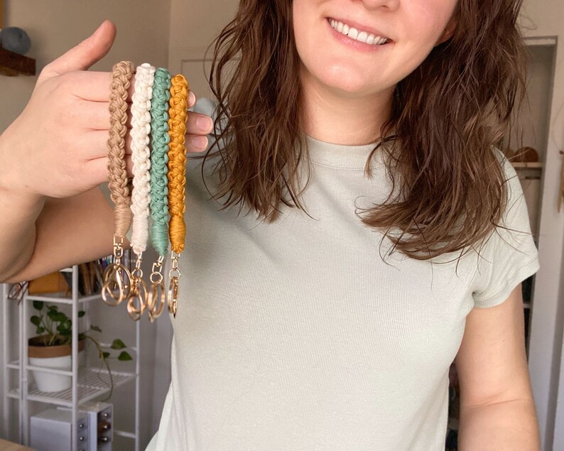 May include: Five colorful braided keychains with gold key rings. The keychains are in shades of brown, cream, green, and yellow.